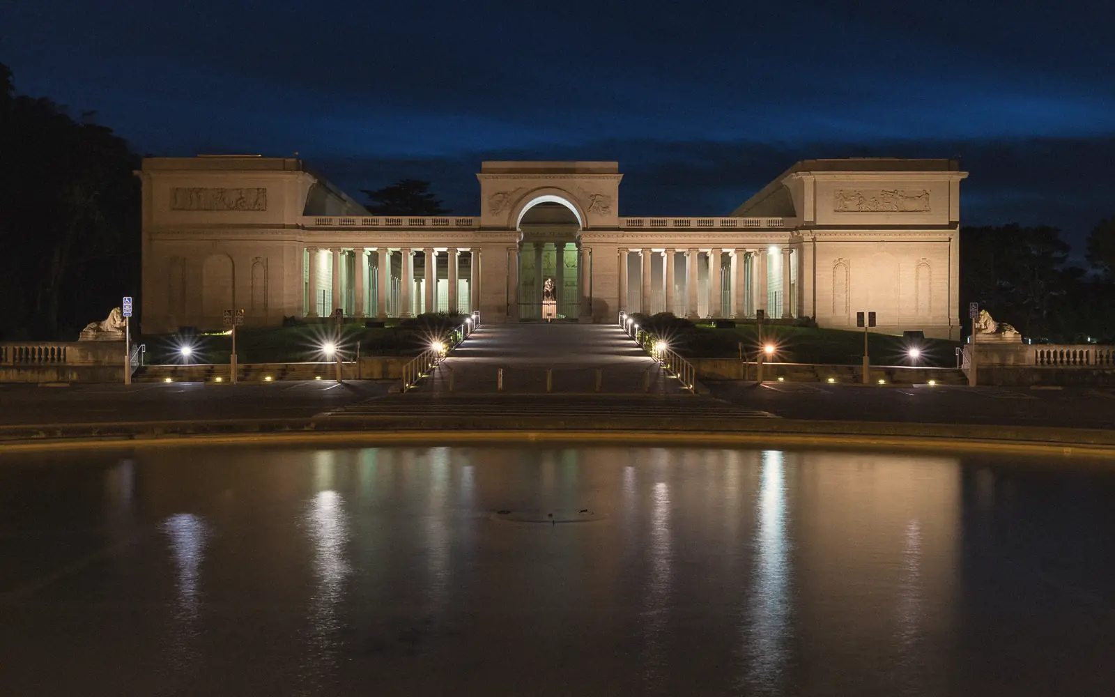 Photo of the Legion of Honor lit up at night above its reflecting pool